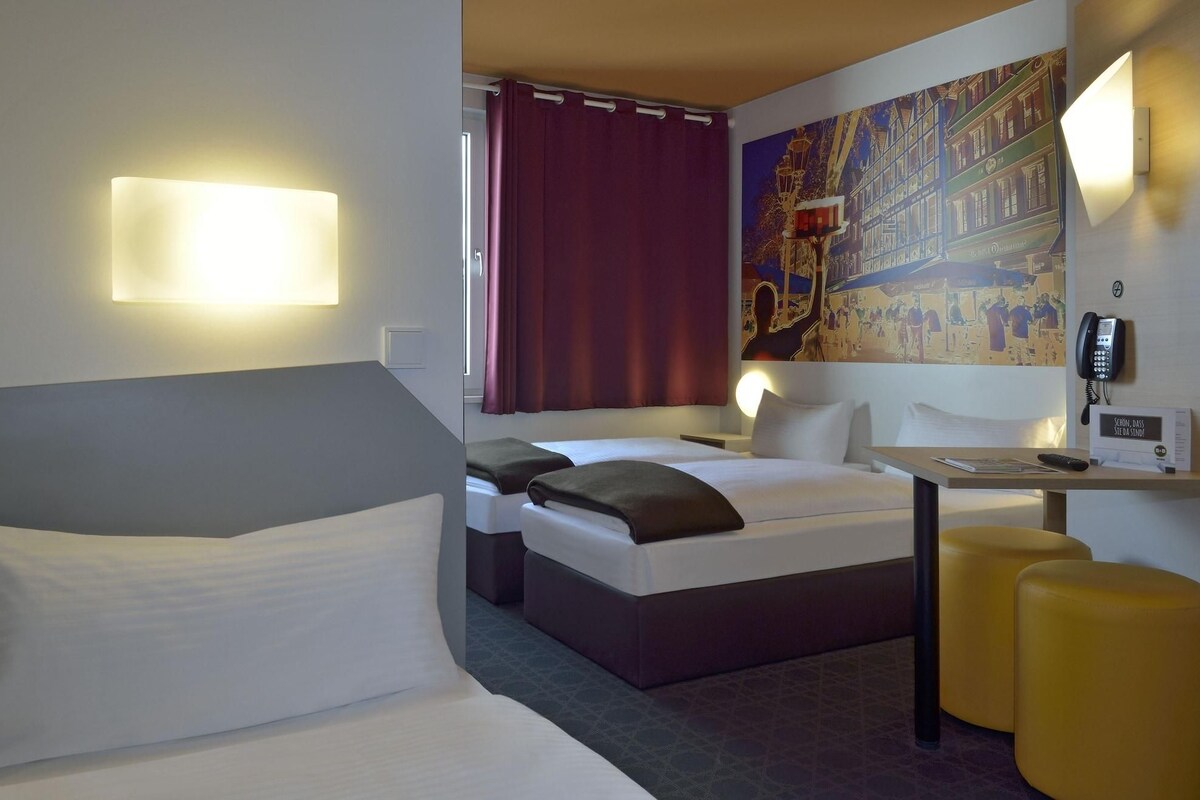 Une chambre d’hôtel avec un lit, un bureau, une chaise, un téléphone et un tableau au mur.