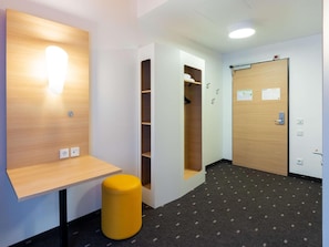 Un couloir avec un bureau en bois, un tabouret jaune, une armoire et une porte avec une pancarte.