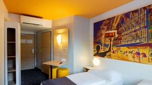 Une chambre d’hôtel avec un lit, un bureau, une chaise, une armoire et un grand tableau au mur.