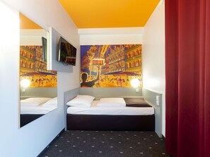 Une petite chambre d’hôtel avec deux lits, une télévision et une fresque représentant un paysage urbain sur le mur.