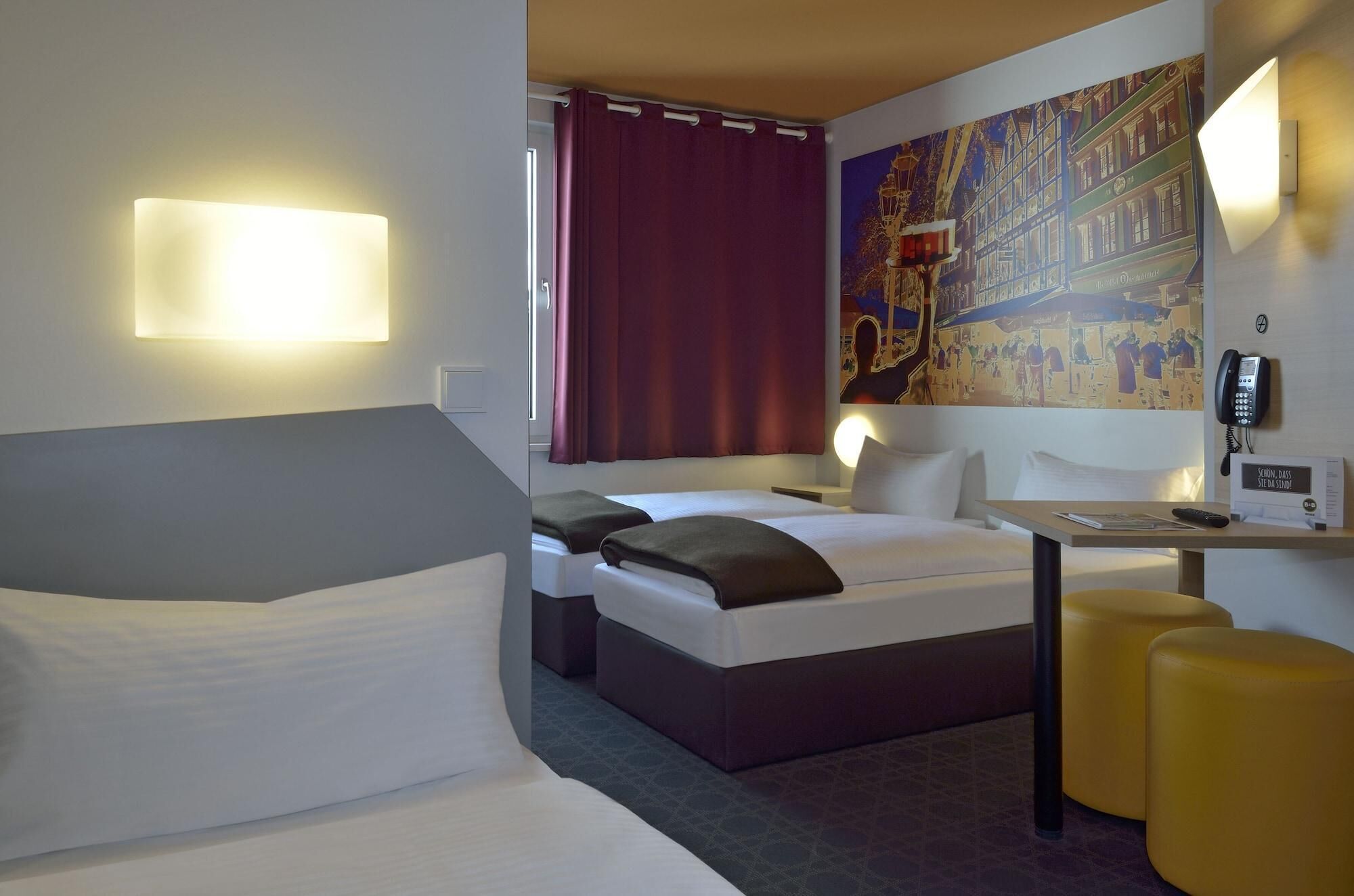 A hotel room with a bed, a desk, a phone, and a painting on the wall.