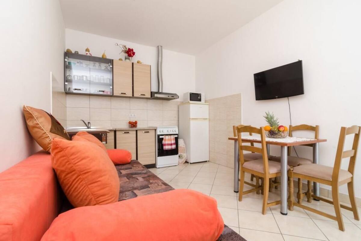 A compact living space with a kitchenette, a dining area, and a flat-screen TV mounted on the wall.