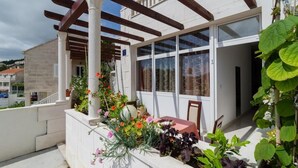 En balkon med et trætag, et bord med rødt dug og flere krukker med planter.
