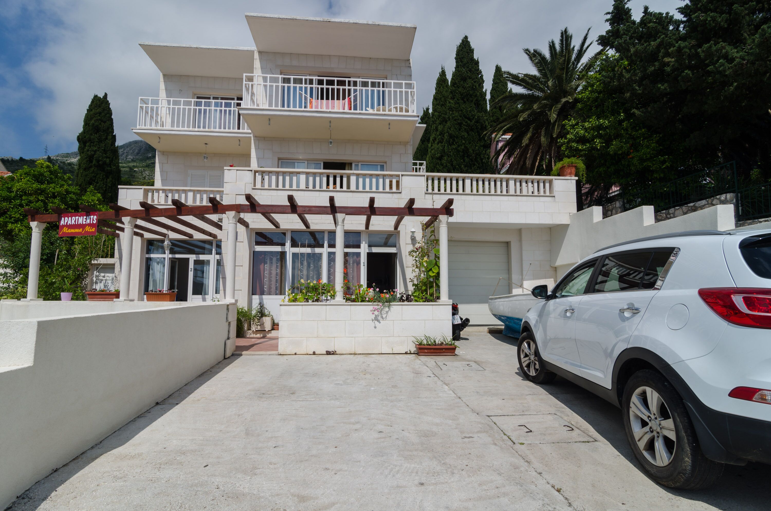 Un edificio de dos pisos con entrada cubierta, un coche estacionado adelante y un cartel que indica que es un complejo de apartamentos.