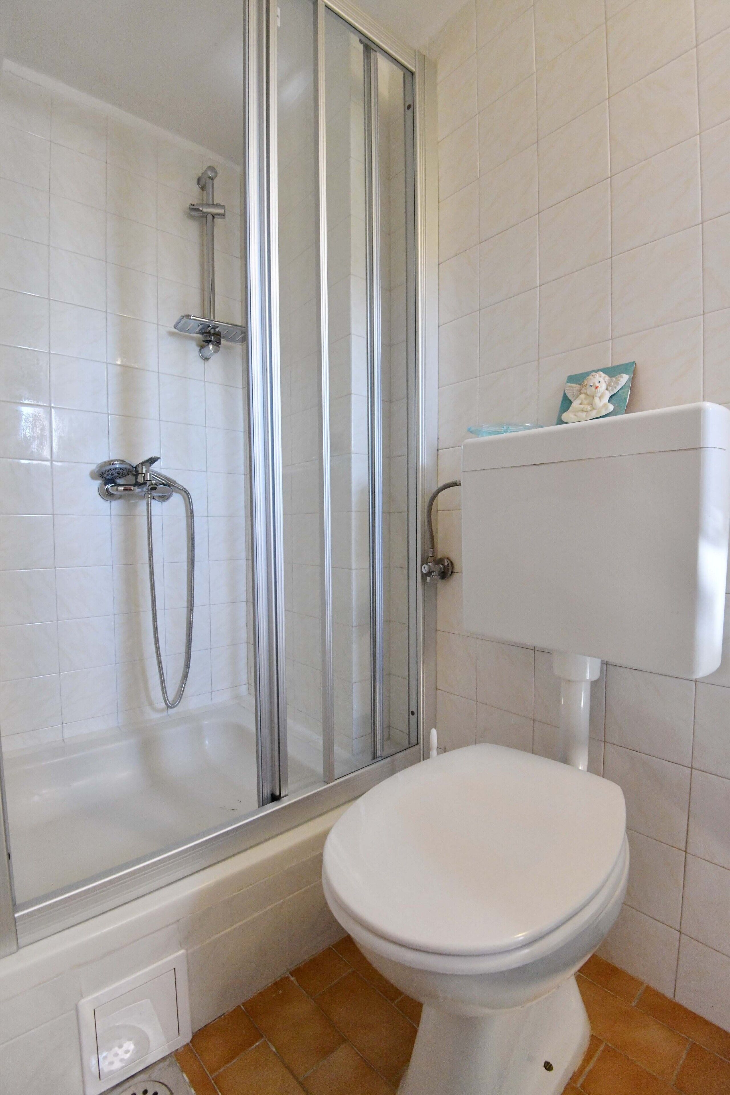 Un baño con ducha de vidrio, inodoro blanco y piso de baldosas.