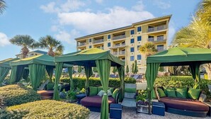 A resort with outdoor seating areas, palm trees, and a building with balconies. - Hilton Head | Island Beach Stay | Pool & Beach | 2BR (Hilton Head)