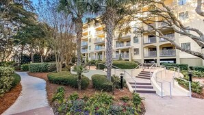 A multi-story hotel with a central courtyard, a curved pathway, and a staircase leading to the upper floors. - Hilton Head | Island Beach Stay | Pool & Beach | 2BR (Hilton Head)