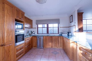 A kitchen with wooden cabinets, a stainless steel dishwasher, and a window with blinds.