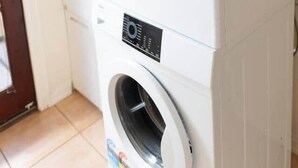 Une machine à laver et un sèche-linge superposés dans une pièce dotée d’une porte et d’un panneau indiquant la sortie sur le mur.