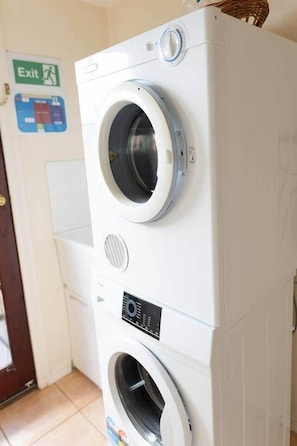 A stacked washer and dryer unit in a room with a door and an exit sign on the wall.