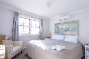 Une chambre d’hôtel avec un grand lit, une chaise, un tableau et une fenêtre avec des rideaux.