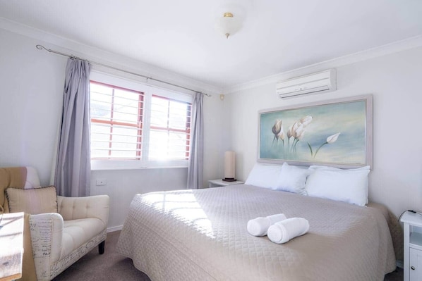 A hotel room with a large bed, a chair, a painting, and a window with curtains.