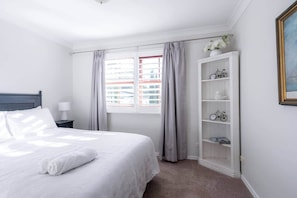 A hotel room with a bed, a nightstand, a window with curtains, a bookshelf with bicycles, and a framed picture on the wall.