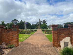 A paved pathway leading to a monument, surrounded by brick walls and greenery.