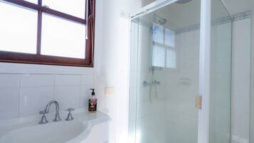 A bathroom with a glass-enclosed shower, a white sink with two faucets, and a window above the sink.