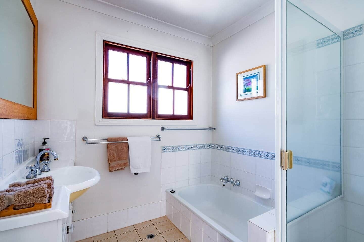 Ein Badezimmer mit weißem Waschbecken, einer Badewanne, einem Fenster und einer Duschkabine.