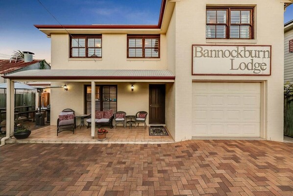 A two-story building with a sign reading "Barnockburn Lodge." There is a covered patio with outdoor furniture and a garage.