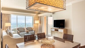 A hotel room with a sofa, chairs, a dining table, a TV, and a balcony with a view.