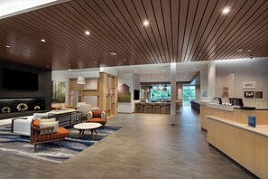 Un hall d’entrée spacieux au design moderne, comprenant un espace détente avec des canapés et des fauteuils, un coin cuisine et un comptoir d’accueil.