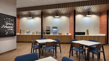 A modern restaurant with a kitchen area, wooden cabinets, and blue chairs around white tables.