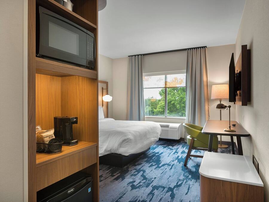 A hotel room with a bed, a desk, a chair, a TV, a coffee maker, and a window with curtains.