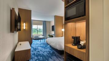 Habitación de hotel con cama, escritorio, microondas, cafetera y vistas al exterior.