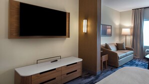 A hotel room with a large flat-screen TV mounted on the wall, a wooden desk with drawers, a sofa, and a small side table. - Fairfield Inn & Suites by Marriott Statesville (Statesville)