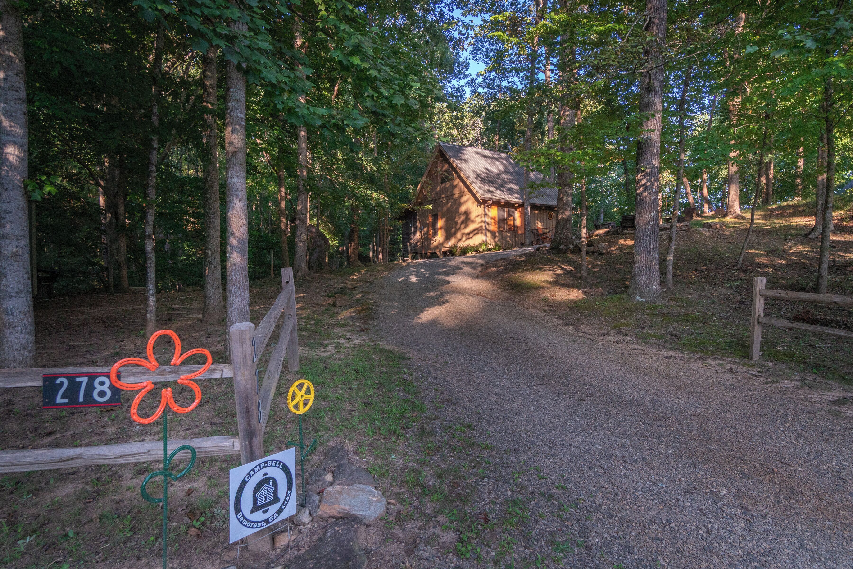 Un rustico chalet circondato da un bosco, con un vialetto sterrato che vi conduce.