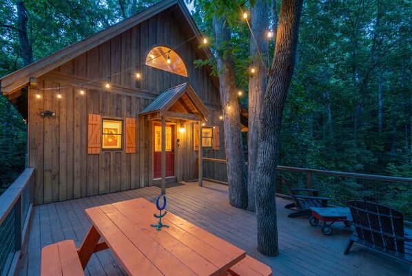 Una cabaña de madera con terraza, luces de cadena y una mesa de picnic.