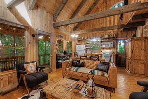 A cozy cabin interior with a wooden interior, a sofa, a dining table, and a kitchen area. - Camp Bell at Twin Rivers |Cozy Riverfront Cabin (Demorest)