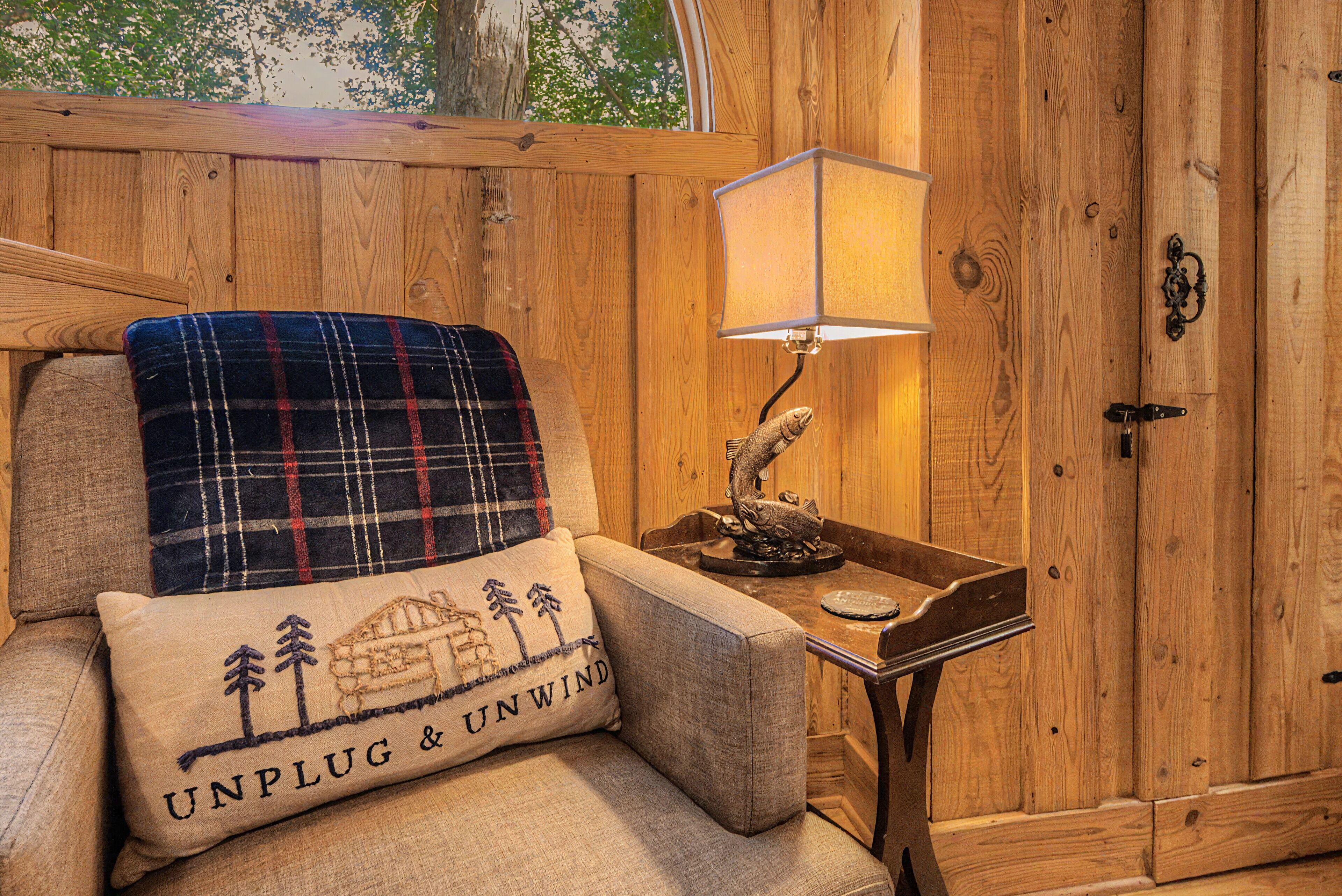 Een knus interieur met houten details, een geruit plaid op een stoel, een lamp en een deur met een handgreep.