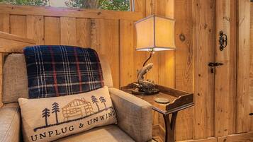 Een knus interieur met houten details, een geruit plaid op een stoel, een lamp en een deur met een handgreep.