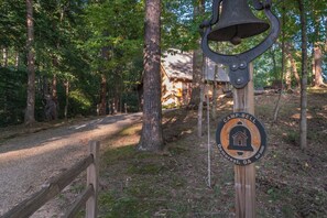 A wooden signpost with a bell and a circular emblem indicating a camp named Camp-Bell in DeNorest, GA, established in 2020. - Camp Bell at Twin Rivers |Cozy Riverfront Cabin (Demorest)