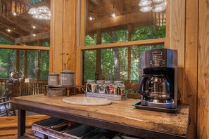 Interior de madera con cafetera, teteras y frascos etiquetados con azúcar y café.
