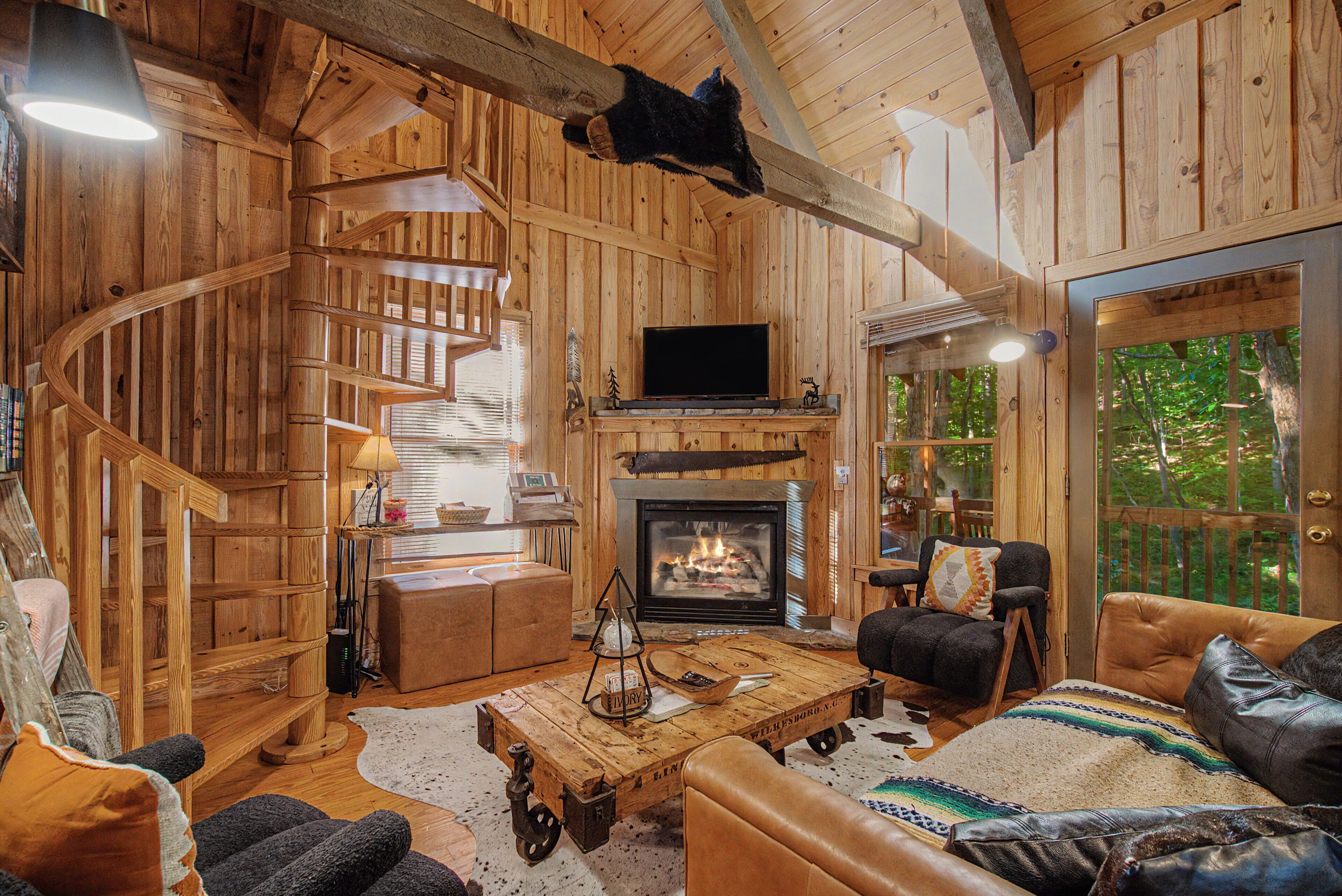 Un intérieur rustique avec un escalier en bois, une cheminée, des meubles en cuir et un téléviseur.