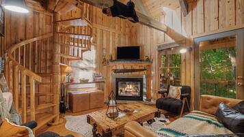 Un intérieur rustique avec un escalier en bois, une cheminée, des meubles en cuir et un téléviseur.