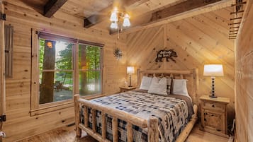 Een slaapkamer in een blokhut met een groot bed, twee bedlampen, een houten hoofdeinde en een raam met uitzicht op bomen.