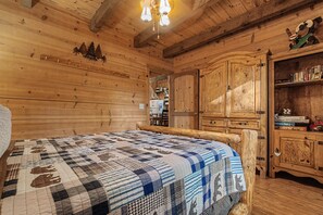 A wooden cabin interior with a bed, a wooden wardrobe, and a shelf with books. - Camp Bell at Twin Rivers |Cozy Riverfront Cabin (Demorest)