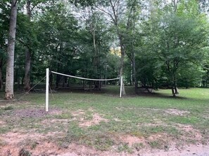 A volleyball net in a wooded area with trees and grass.
