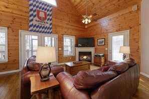 A wooden-paneled room with leather sofas, a fireplace, and a mounted television. - Rest and Be Thankful - Cozy Retreat Near Downtown (Helen)