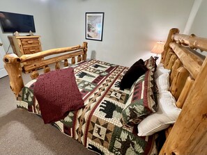 Ein hölzernes Bett mit einer gemusterten Steppdecke, einer roten Tagesdecke und einem Kopfkissen.