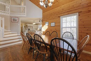 A dining area with a wooden table and chairs, a staircase, and a kitchen in the background. - Rest and Be Thankful - Cozy Retreat Near Downtown (Helen)