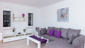Ein modernes Wohnzimmer mit grauem Sofa, weißem Unterhaltungsschrank und einem violetten Couchtisch.