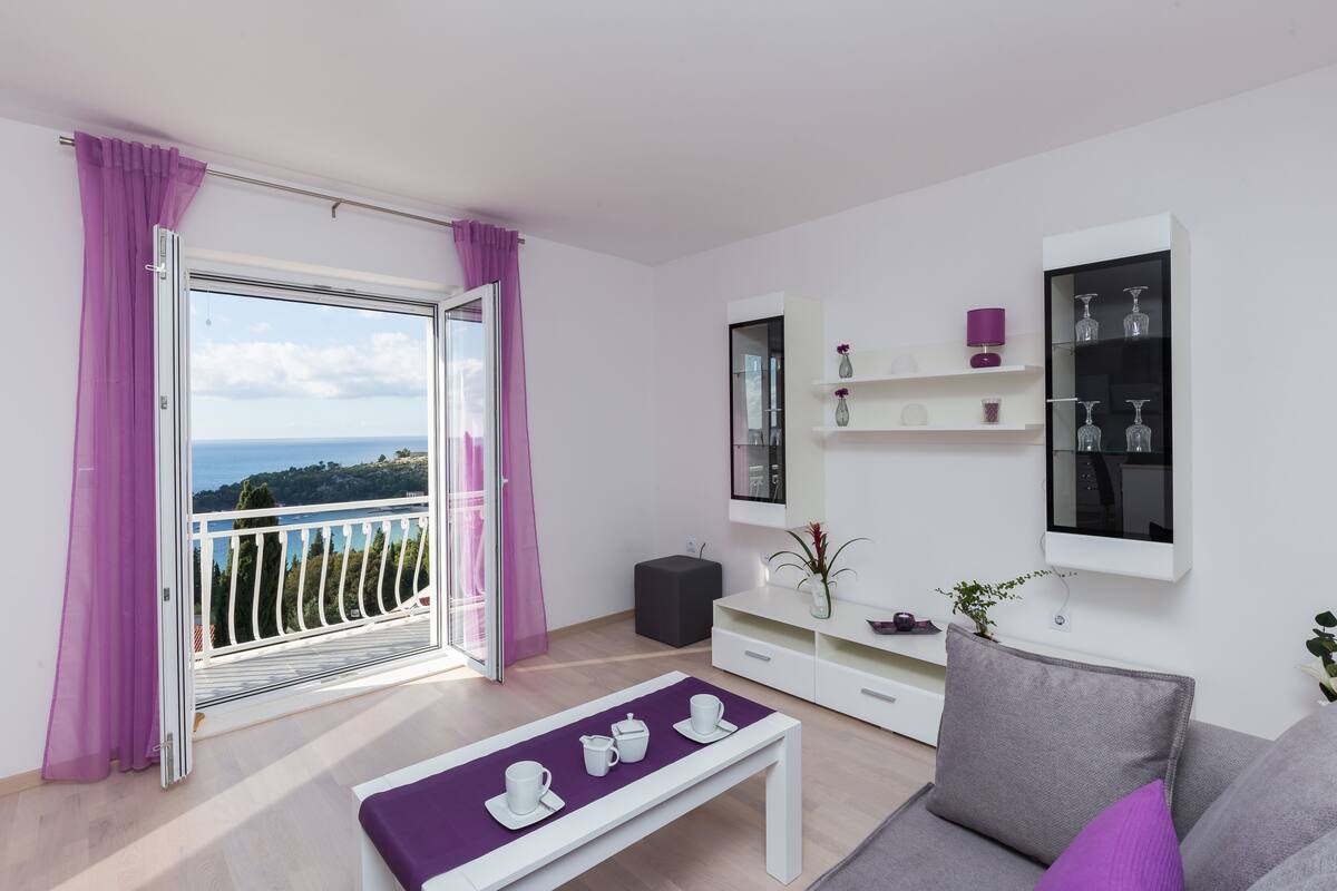 Una sala de estar moderna con balcón, un sofá blanco, una mesa de centro y un televisor montado en la pared.