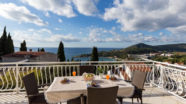 Ein Balkon mit Frühstückstisch, der Blick auf die Küste mit Bergen und eine Stadt in der Ferne gewährt.