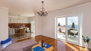 Ein geräumiges Wohnzimmer mit einer Couch, einem Essbereich mit Tisch und Stühlen, einer Küche und einem Balkon mit Meerblick.
