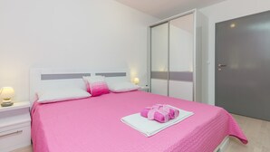 Ein ordentlich bezogenes Bett mit rosa Bettwäsche, einem weißen Kissen und einem rosafarbenen Handtuch auf einem weißen Nachttisch.