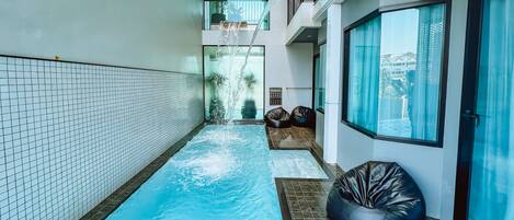 A narrow indoor swimming pool with tiled walls and a black bean bag chair.