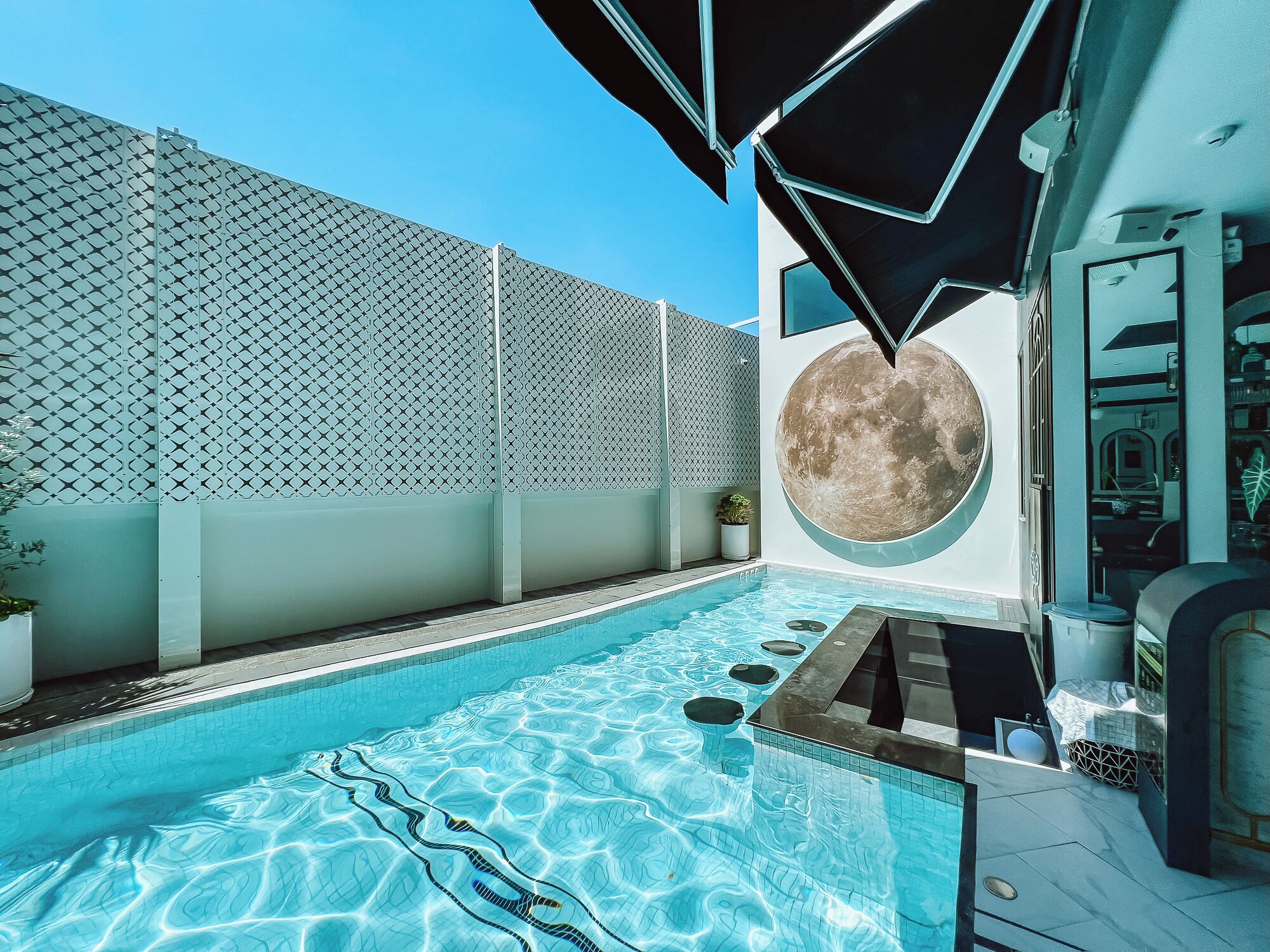 Un espace piscine extérieur moderne, doté d’une piscine à l’eau d’un bleu limpide, d’une clôture aux lignes géométriques et d’une grande fenêtre circulaire.