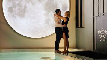 A couple standing by a pool with a large moon projection on the wall.